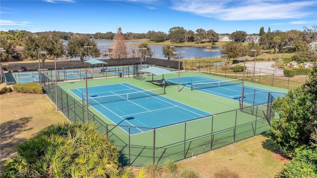 view of tennis court with fence and a water view