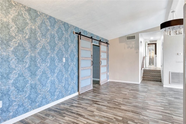 unfurnished room featuring wood-type flooring, lofted ceiling, and a barn door