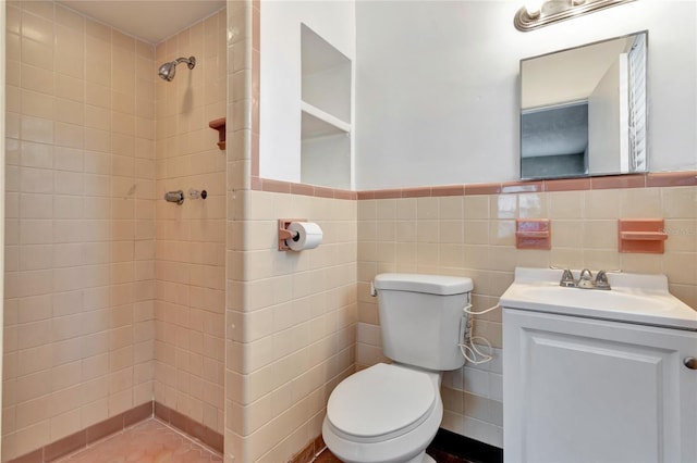 bathroom featuring a tile shower, tile walls, vanity, and toilet