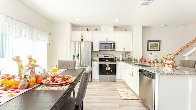 kitchen with appliances with stainless steel finishes, light hardwood / wood-style floors, white cabinetry, light stone countertops, and sink