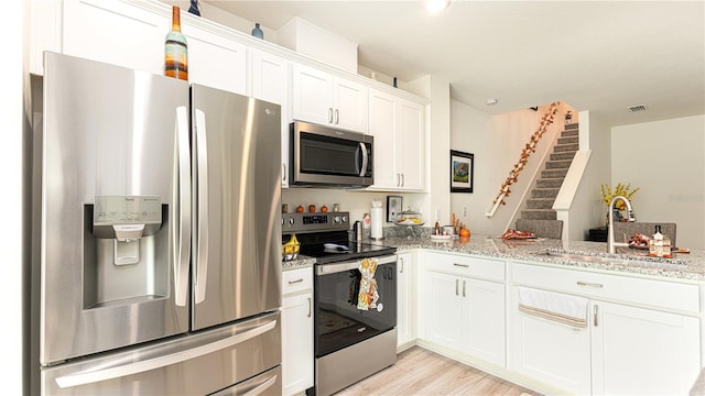 kitchen with light stone counters, white cabinets, sink, appliances with stainless steel finishes, and light hardwood / wood-style floors