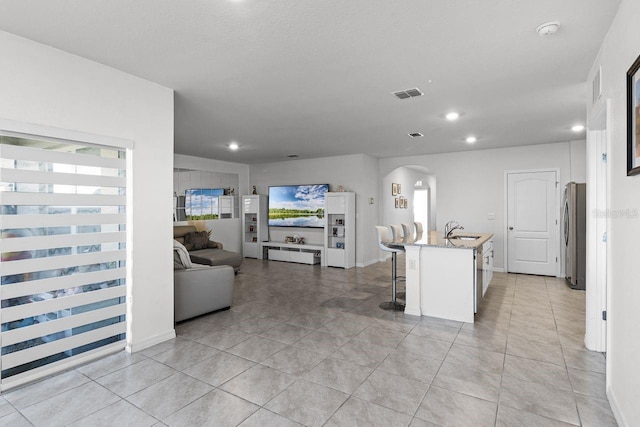 kitchen with white cabinets, sink, light stone countertops, an island with sink, and a kitchen bar