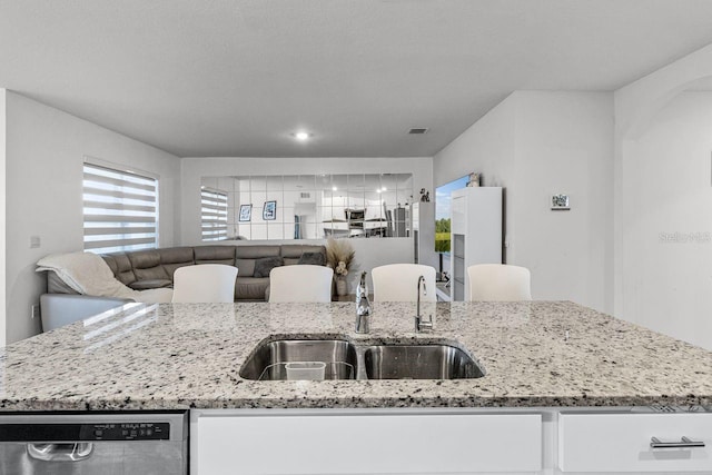 kitchen with light stone countertops, white cabinets, stainless steel dishwasher, and sink