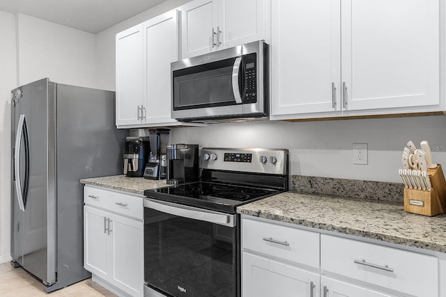 kitchen with light tile patterned flooring, light stone countertops, white cabinets, and stainless steel appliances