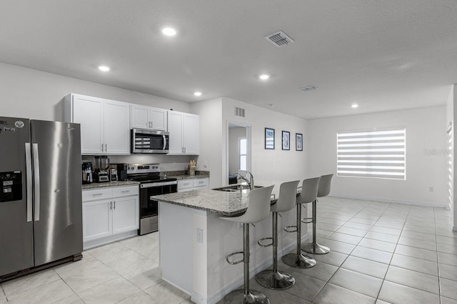 kitchen featuring a center island with sink, white cabinets, sink, light stone counters, and stainless steel appliances