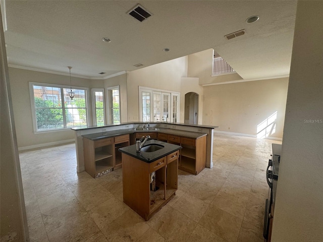 kitchen featuring ornamental molding, a center island with sink, hanging light fixtures, and sink