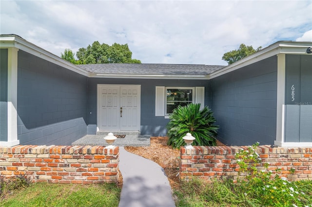 entrance to property with covered porch, roof with shingles, and concrete block siding