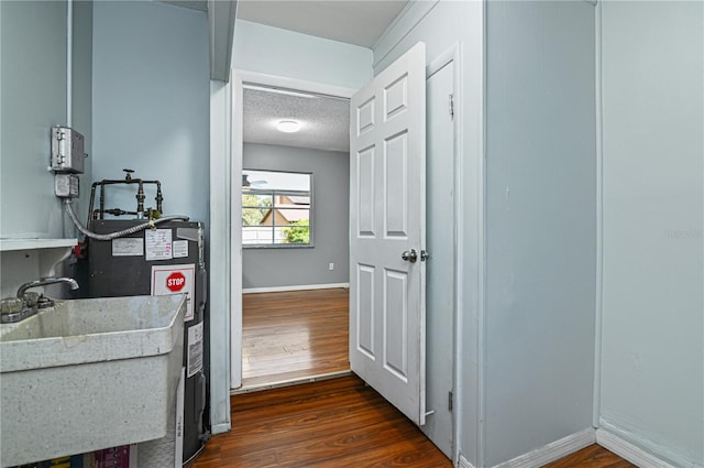 hallway with dark wood-style flooring, a sink, a textured ceiling, and baseboards