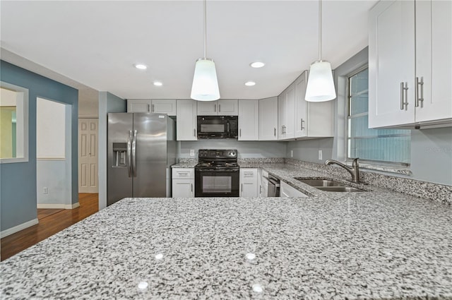 kitchen with dark wood finished floors, a sink, black appliances, light stone countertops, and baseboards