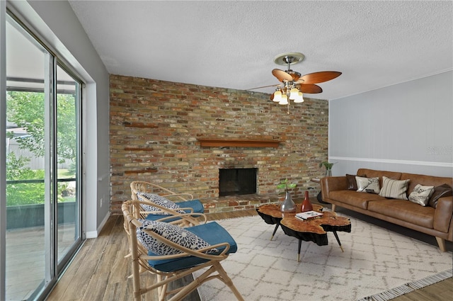 living area featuring a textured ceiling, ceiling fan, wood finished floors, baseboards, and a brick fireplace