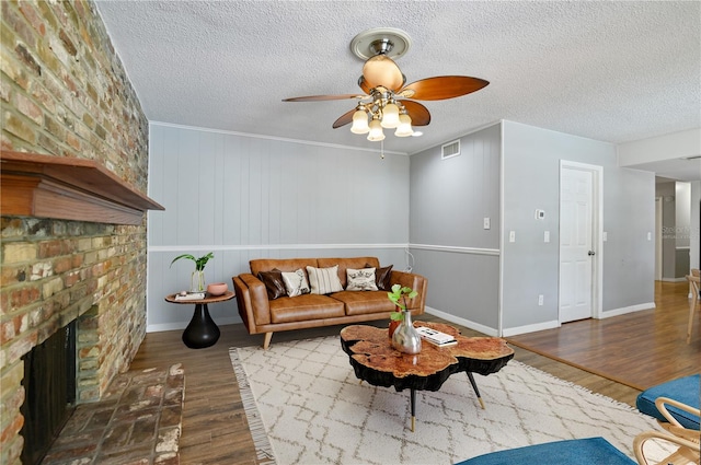 living room featuring a fireplace, visible vents, a ceiling fan, a textured ceiling, and wood finished floors