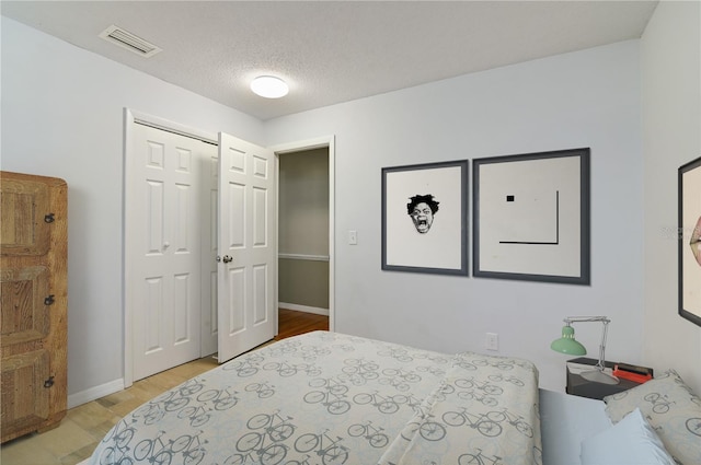 bedroom featuring light wood-style floors, baseboards, visible vents, and a textured ceiling