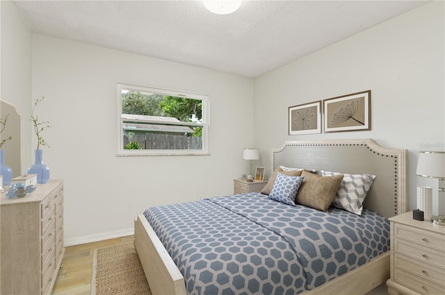 bedroom featuring a textured ceiling, light wood-style flooring, and baseboards