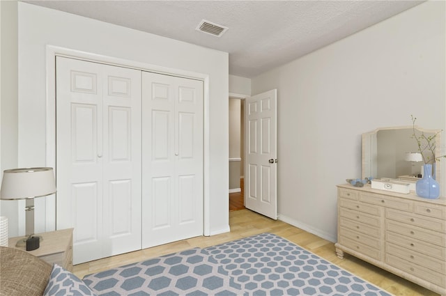 bedroom with a textured ceiling, a closet, wood finished floors, and visible vents