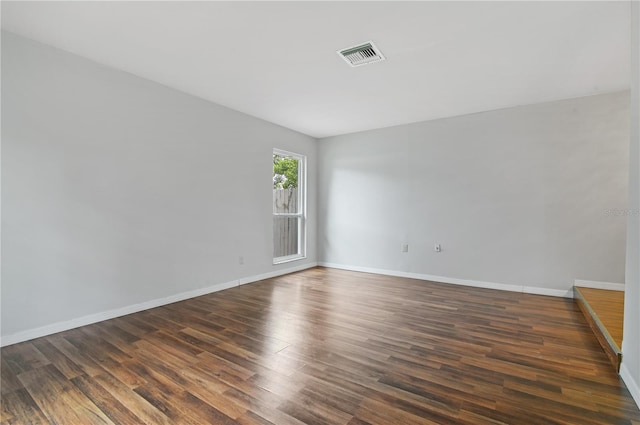 spare room with dark wood-style flooring, visible vents, and baseboards