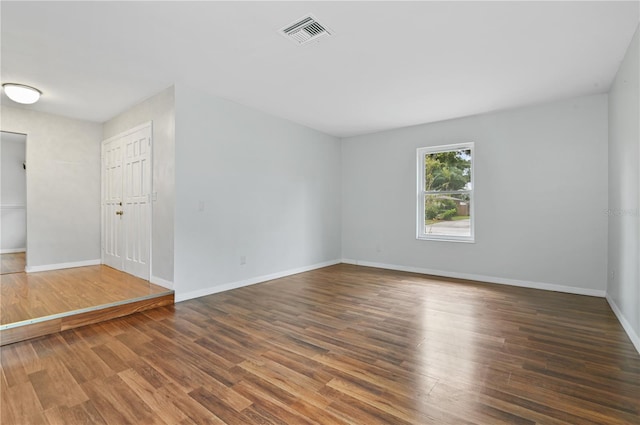 empty room with wood finished floors, visible vents, and baseboards