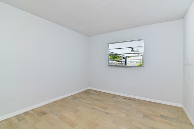 spare room with light wood-type flooring, baseboards, and a textured ceiling