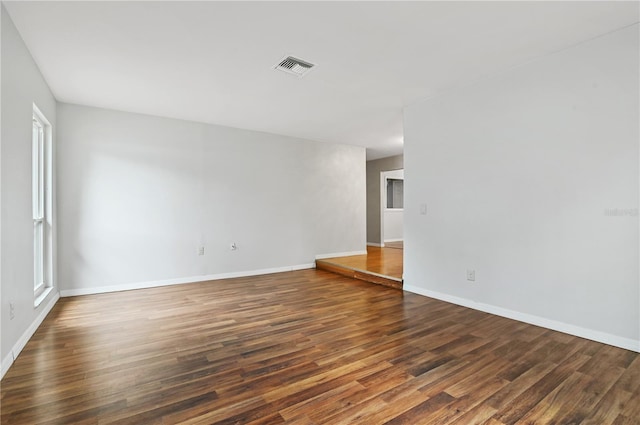 empty room with dark wood finished floors, visible vents, and baseboards