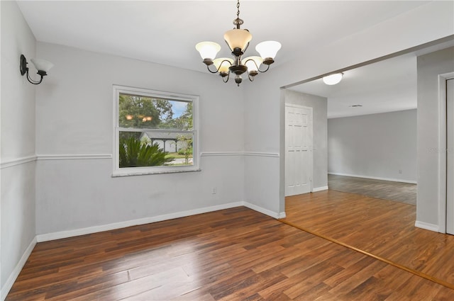 empty room featuring an inviting chandelier, wood finished floors, and baseboards