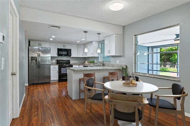 kitchen with dark wood-style floors, black appliances, a peninsula, and light stone countertops