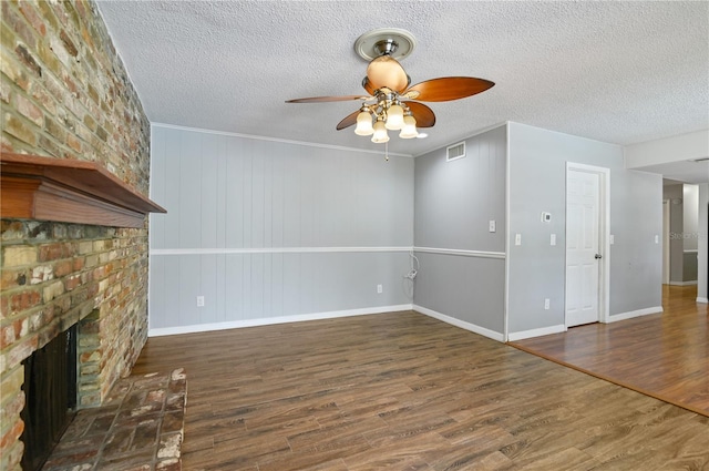 unfurnished living room with a brick fireplace, visible vents, a textured ceiling, and wood finished floors