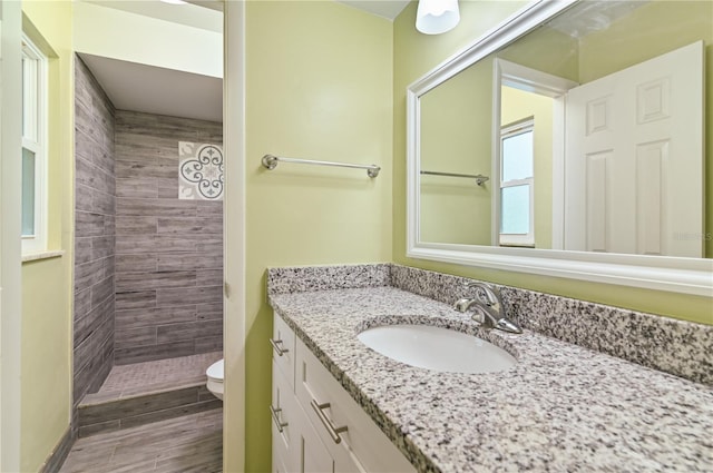 bathroom featuring toilet, wood finished floors, tiled shower, and vanity