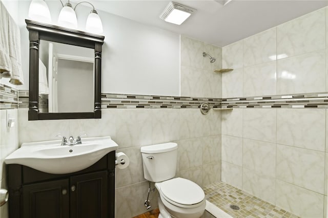 bathroom with tile walls, tiled shower, vanity, and toilet