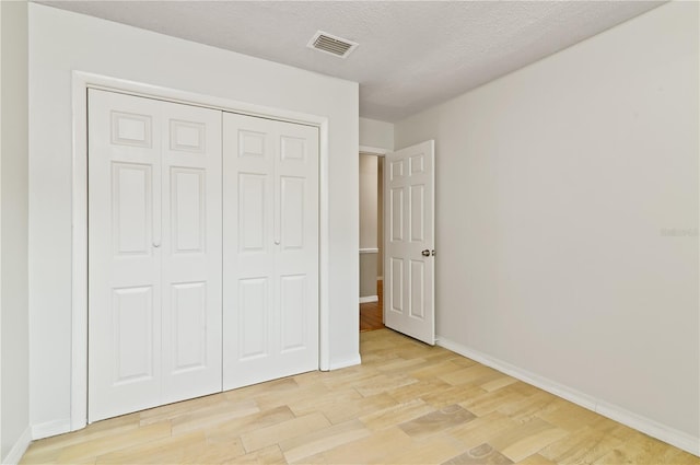 unfurnished bedroom featuring baseboards, visible vents, light wood-style flooring, a textured ceiling, and a closet