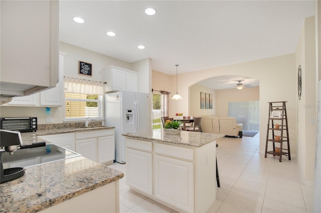 kitchen featuring decorative light fixtures, a center island, white refrigerator with ice dispenser, and white cabinets