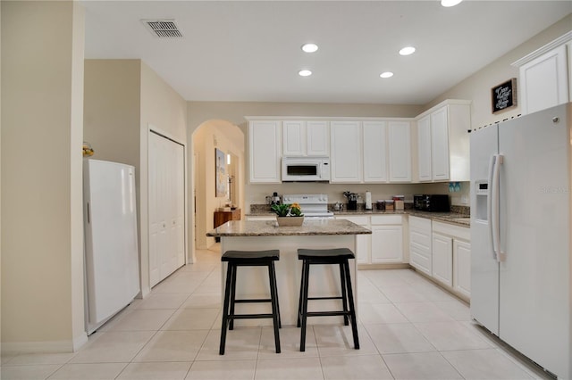 kitchen with light stone countertops, white cabinetry, white appliances, and a kitchen island