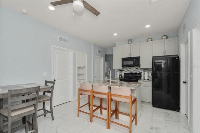 kitchen with black appliances, white cabinetry, an island with sink, and light stone counters