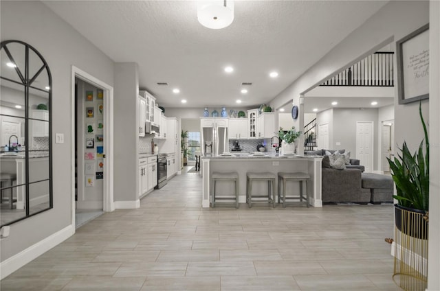 kitchen with tasteful backsplash, a textured ceiling, a breakfast bar area, white cabinets, and appliances with stainless steel finishes