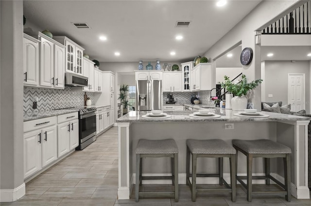 kitchen featuring light stone countertops, a kitchen breakfast bar, kitchen peninsula, white cabinets, and appliances with stainless steel finishes