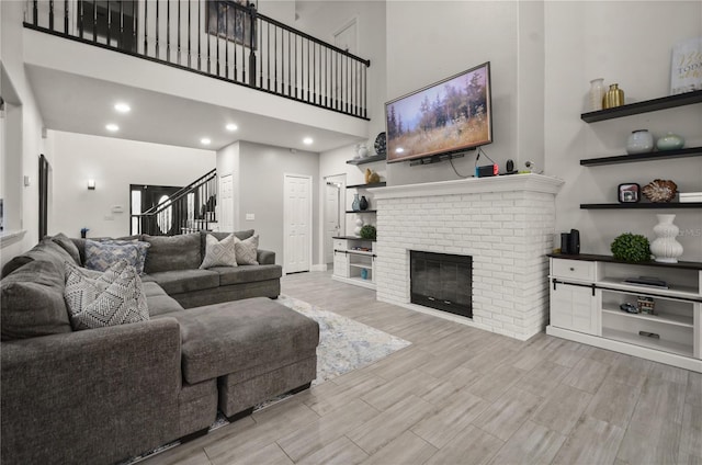 living room featuring a high ceiling, light wood-type flooring, and a brick fireplace