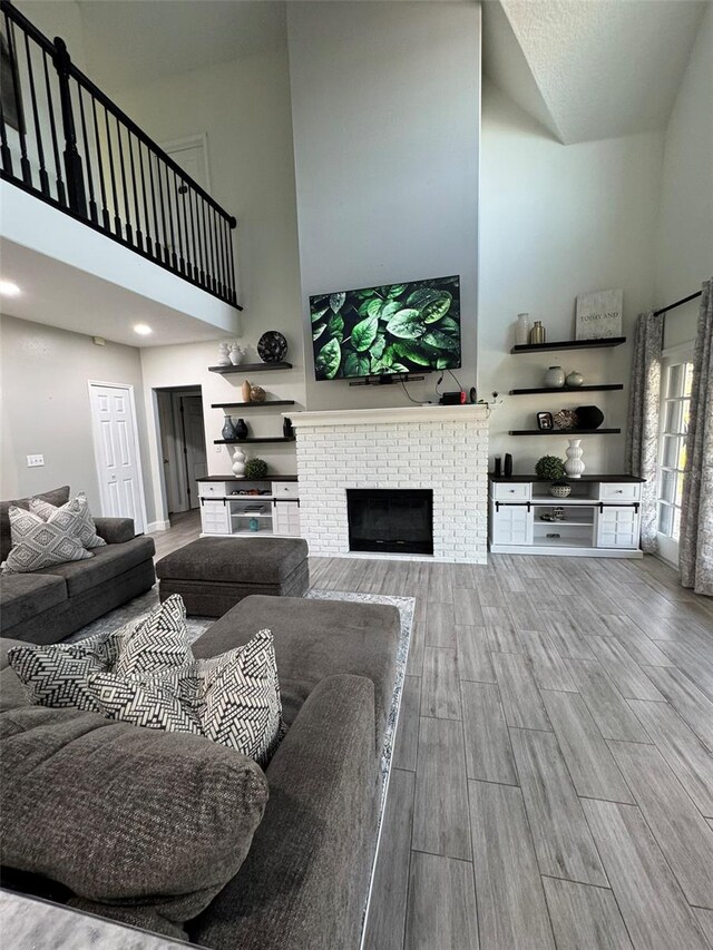 living room with hardwood / wood-style floors, a towering ceiling, and a brick fireplace