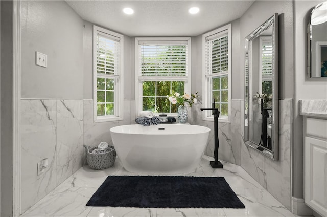 bathroom with a tub, tile walls, vanity, and a textured ceiling