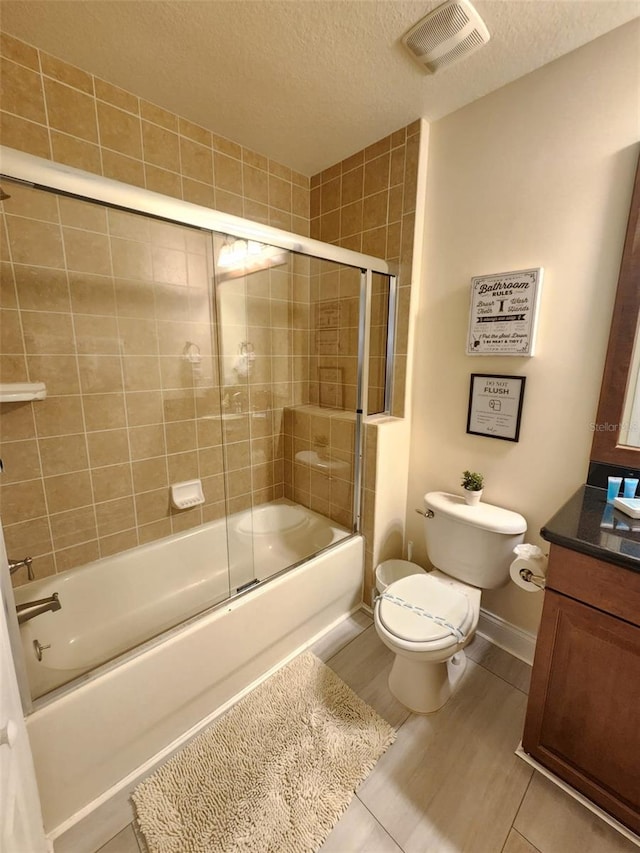 full bathroom with tile patterned floors, bath / shower combo with glass door, a textured ceiling, toilet, and vanity