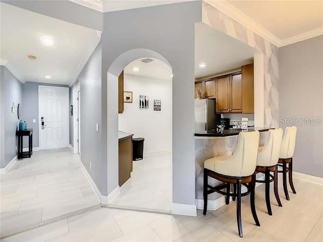 kitchen with a kitchen bar, stainless steel fridge, and ornamental molding