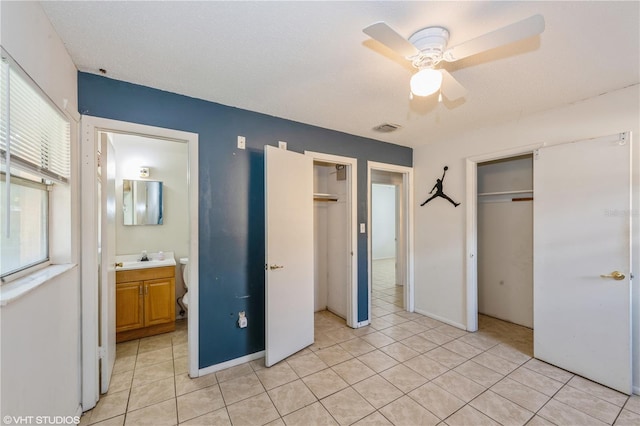 unfurnished bedroom featuring connected bathroom, light tile patterned flooring, ceiling fan, and multiple closets