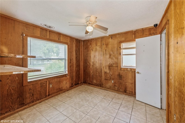 empty room with ceiling fan, a textured ceiling, and wood walls