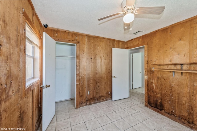 unfurnished bedroom featuring a closet, a textured ceiling, light tile patterned flooring, wooden walls, and ceiling fan