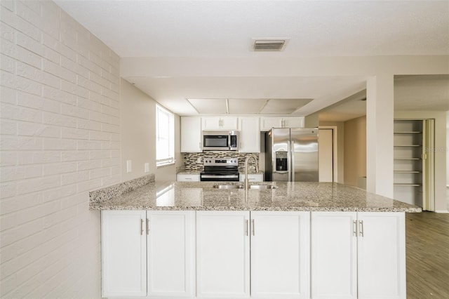 kitchen featuring white cabinets, kitchen peninsula, appliances with stainless steel finishes, hardwood / wood-style floors, and light stone countertops