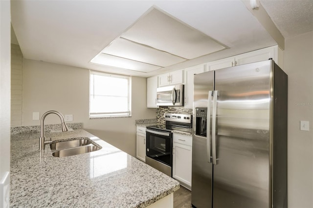 kitchen featuring appliances with stainless steel finishes, white cabinetry, kitchen peninsula, light stone countertops, and sink