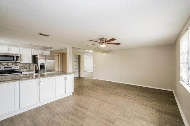 kitchen with light hardwood / wood-style floors, white cabinetry, appliances with stainless steel finishes, light stone countertops, and ceiling fan