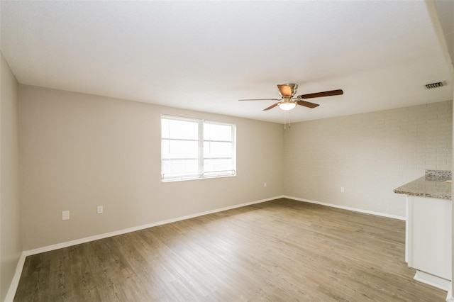 empty room with light wood-type flooring, ceiling fan, and brick wall