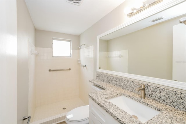 bathroom with a tile shower, vanity, and toilet