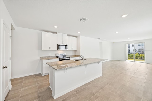 kitchen featuring light stone countertops, a kitchen breakfast bar, a kitchen island with sink, white cabinets, and appliances with stainless steel finishes