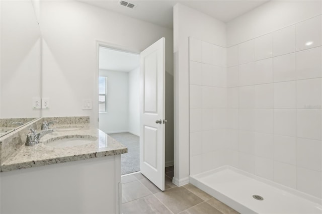 full bath with visible vents, tiled shower, double vanity, a sink, and tile patterned flooring