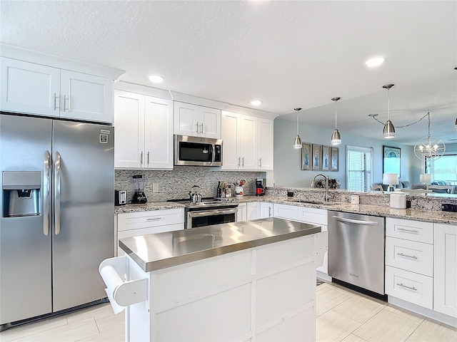 kitchen featuring white cabinets, appliances with stainless steel finishes, hanging light fixtures, and kitchen peninsula