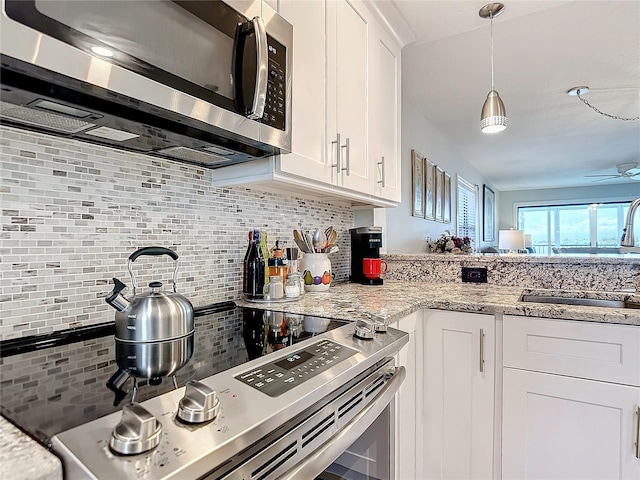 kitchen featuring tasteful backsplash, white cabinets, light stone countertops, stainless steel appliances, and sink